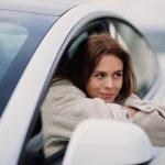 woman in gray coat leaning on white car