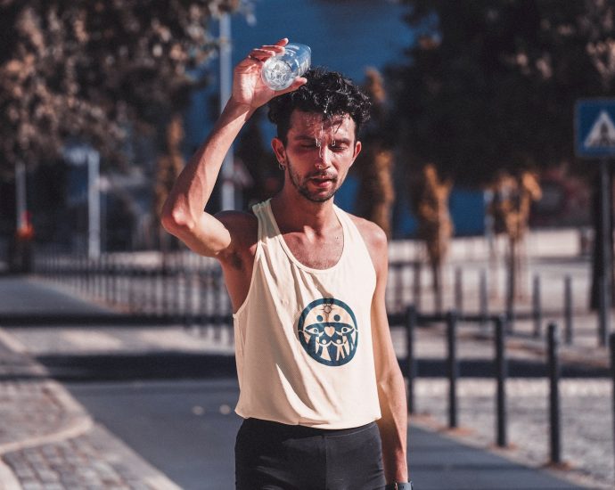 Exhausted muscular sportsman pouring water on head after running in sunny day in park