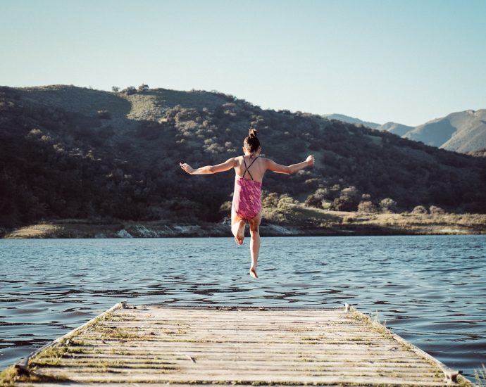 woman wearing pink top jumping towards water during daytime