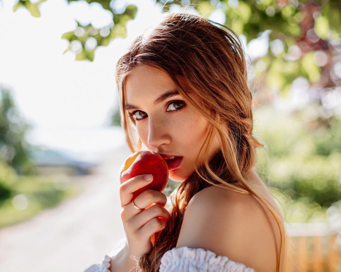 woman in white off shoulder shirt holding red apple