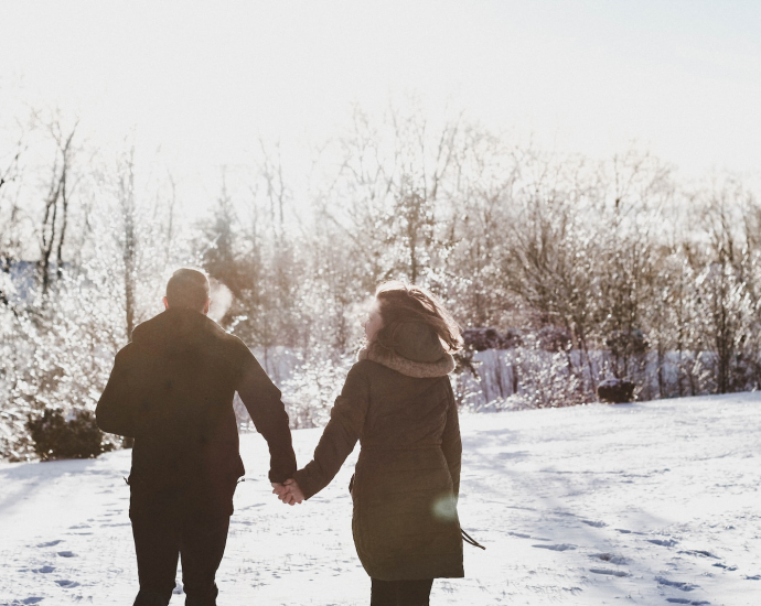 couple holding hand while walking on snow covered field