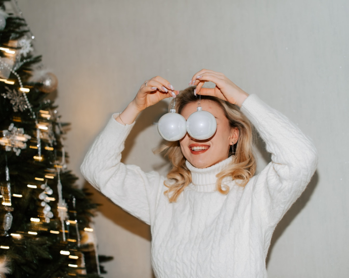 a woman in a white sweater holding two white balls over her eyes