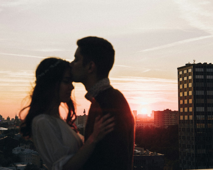 a man and a woman kissing in front of a sunset