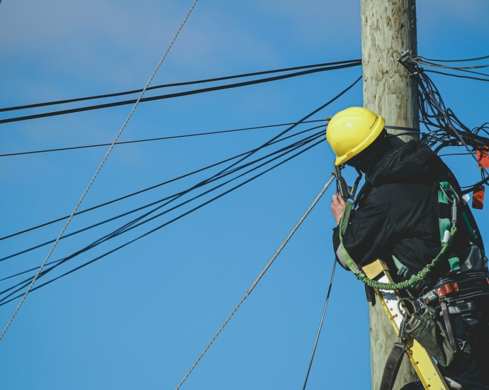 man in black jacket and yellow hard hat climbing on brown wooden post during daytime