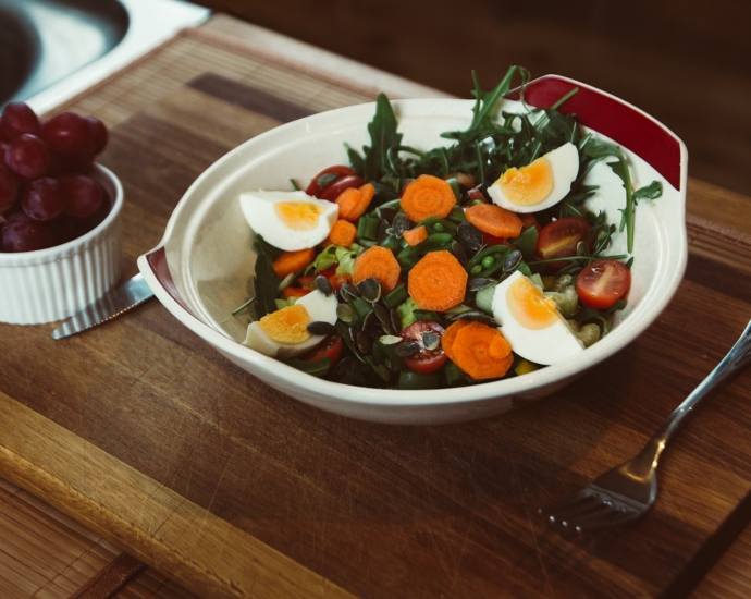 bowl of salad with slide of cooked egg with grapes on the side