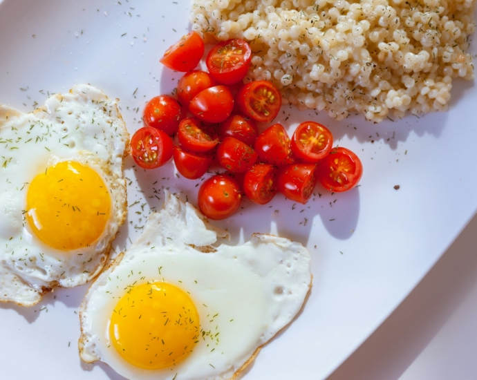 two sunny side eggs with sliced tomatoes on ceramic plate