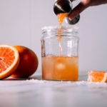 person pours liquid on jar near orange fruits