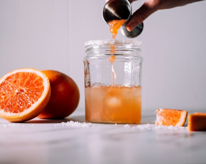 person pours liquid on jar near orange fruits