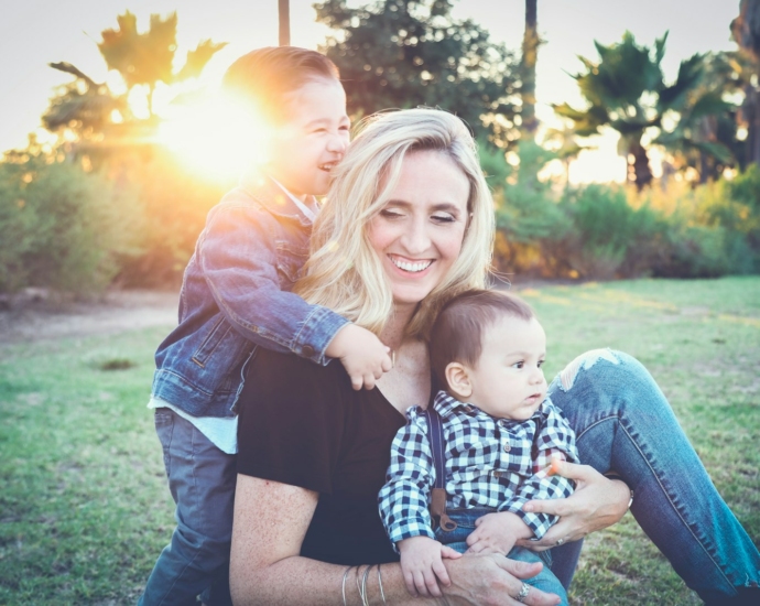 woman holding baby sitting on green grass field under sunset