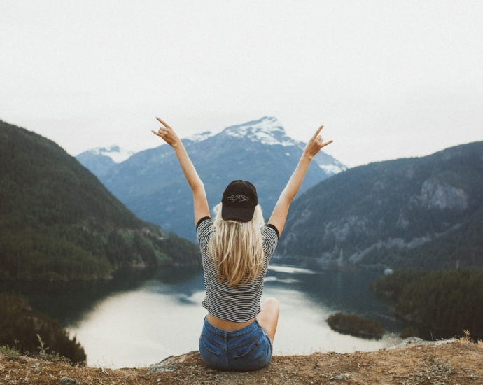 woman sitting on cliff raising both hands