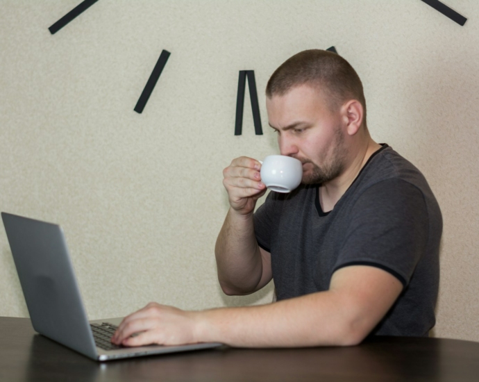 a man drinking a cup of coffee while using a laptop