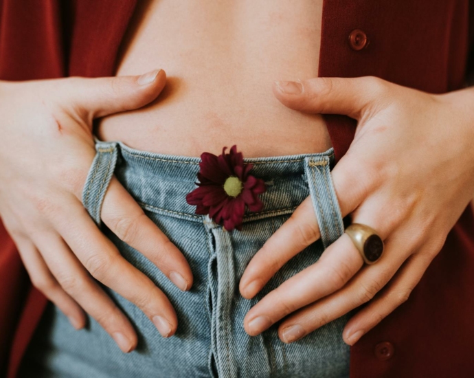 Crop faceless female in casual clothes decorated with blooming flower revealing bare stomach