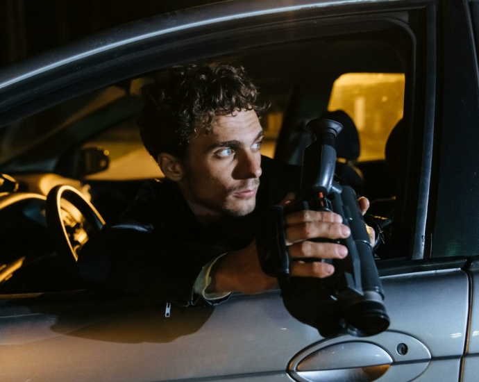 Man Sitting in a Car at Night, Holding a Camcorder and Looking Back through the Window