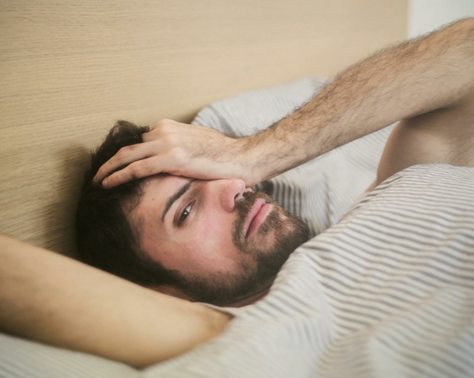 From above of sleepy bearded man just awakened rubbing eyes while lying on bed at home