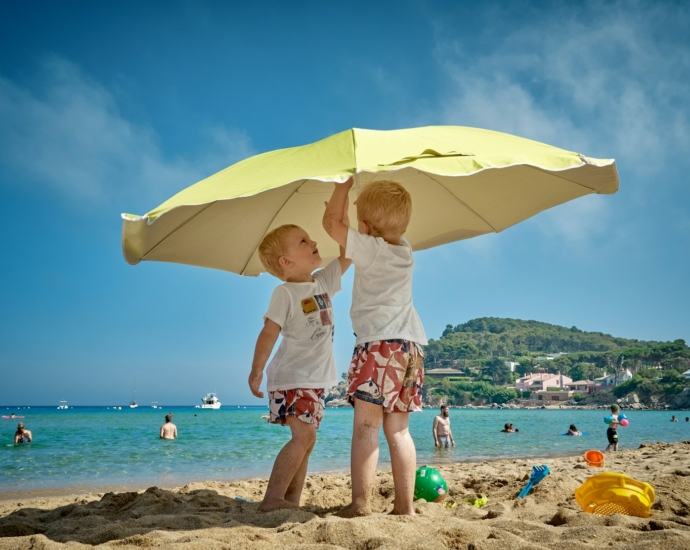 two children playing under umbrella on seashore