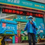 man in blue jacket and blue denim jeans standing beside green and red kanji text store