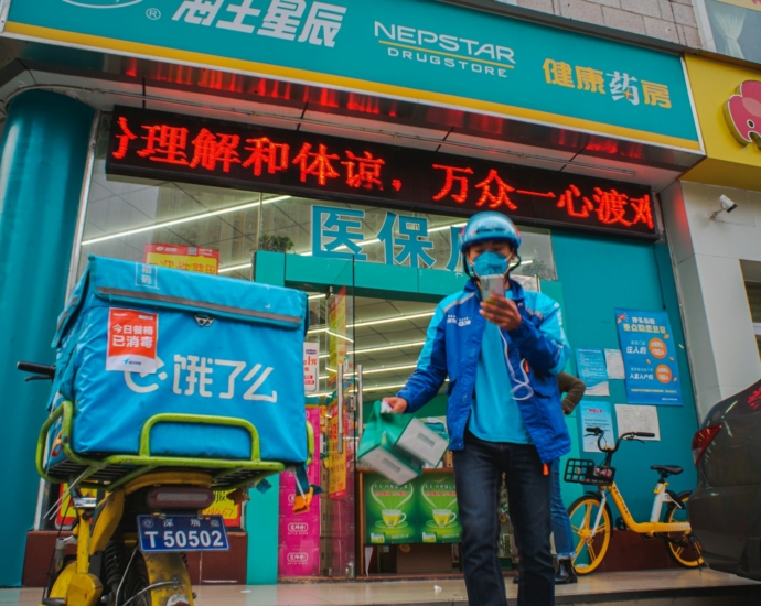 man in blue jacket and blue denim jeans standing beside green and red kanji text store