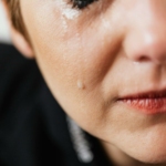 Closeup of crop anonymous sad adult female with makeup crying because of emotional problems