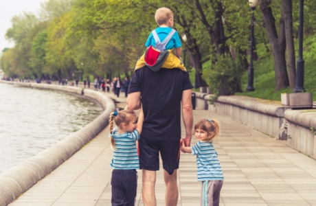 man in black t-shirt and brown shorts holding girl in blue and black jacket walking