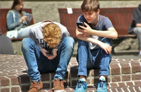 Two teenagers seated outdoors, focused on their smartphones, embracing modern technology.