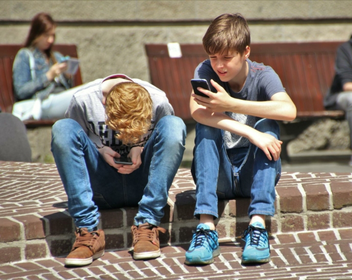 Two teenagers seated outdoors, focused on their smartphones, embracing modern technology.