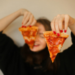 A woman holds two pepperoni pizza slices, focusing on food and fun.