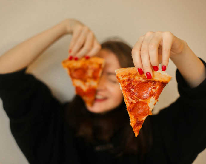 A woman holds two pepperoni pizza slices, focusing on food and fun.