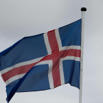 The national flag of Iceland waving atop a flagpole against a cloudy sky.