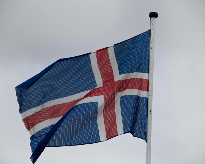 The national flag of Iceland waving atop a flagpole against a cloudy sky.