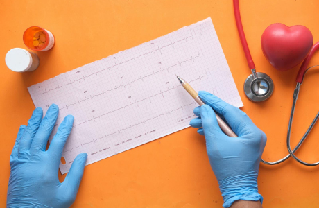 Hands with gloves analyzing an electrocardiogram on an orange background with stethoscope and pills.