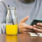 a person holding a phone and a glass of liquid