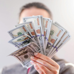 A close-up of a person holding a fan of US dollar bills, signifying wealth and financial success.