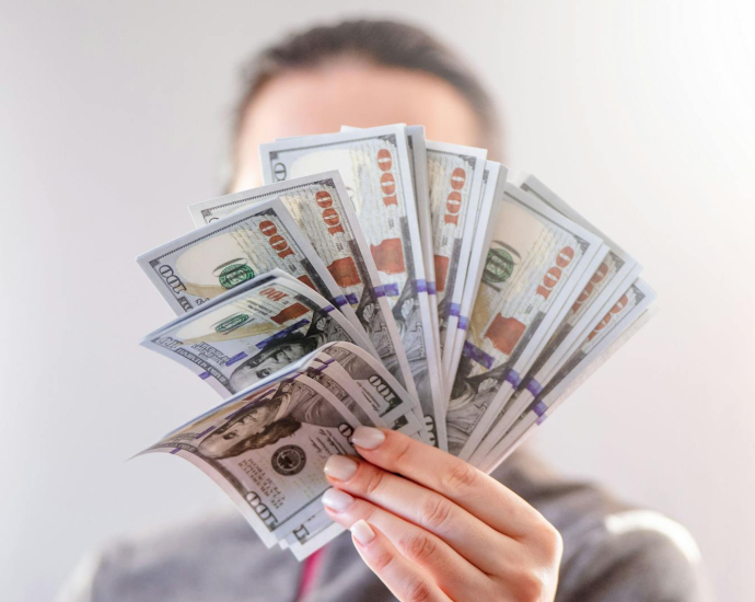 A close-up of a person holding a fan of US dollar bills, signifying wealth and financial success.