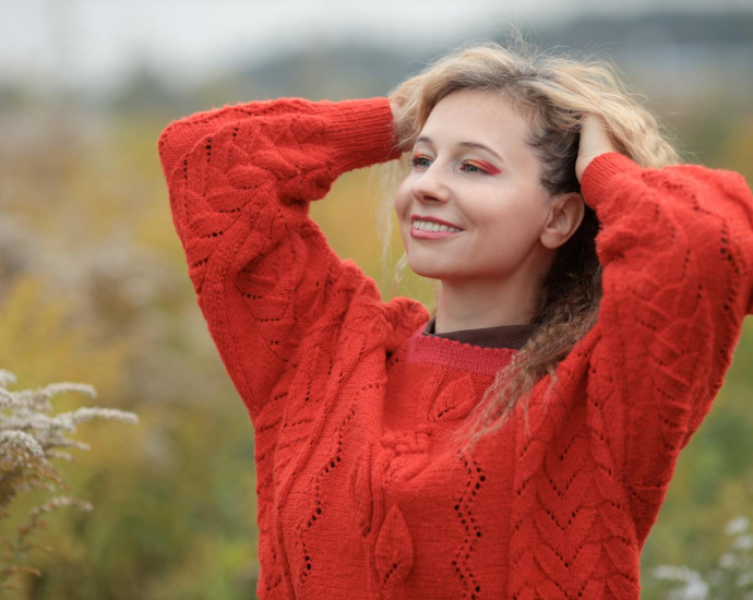 Woman in a red sweater smiling outdoors, enjoying a sunny day in nature.