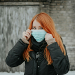 woman in black jacket covering her face with white ceramic mug