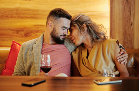 A couple shares an intimate moment with wine glasses at a cozy restaurant setting.