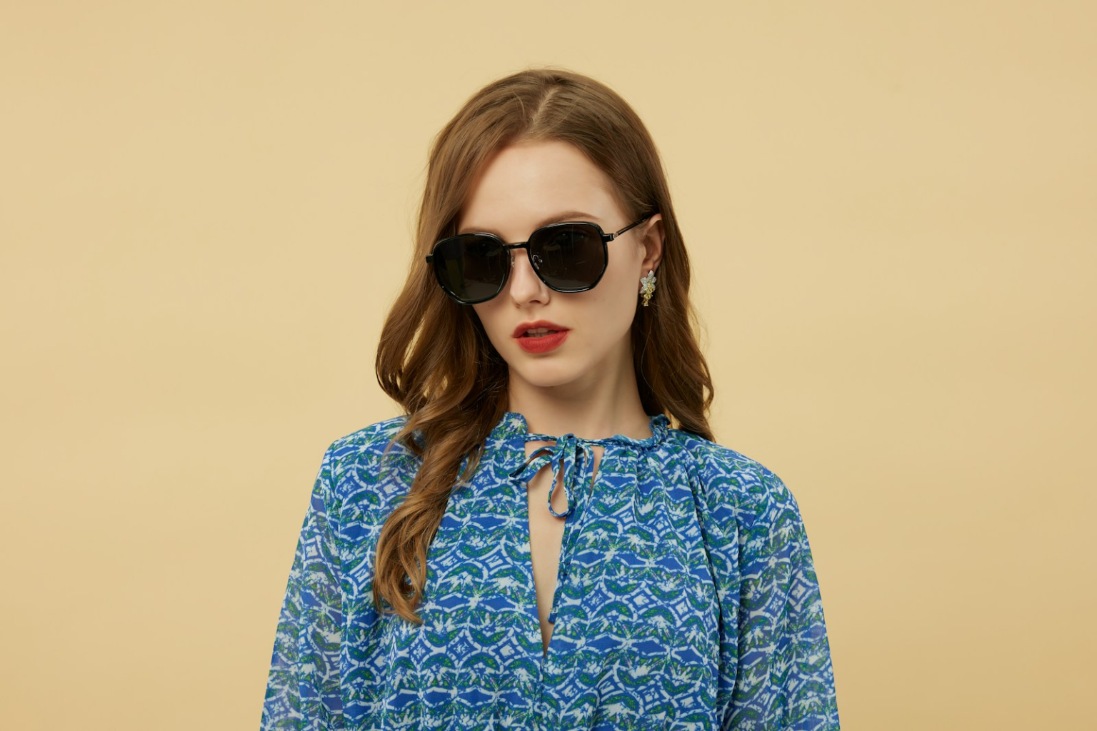 Woman wears sunglasses and a blue patterned dress.