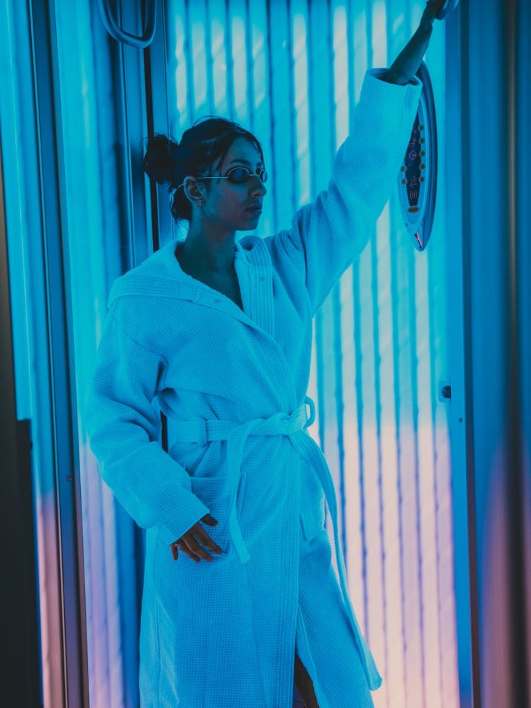 Woman in a bathrobe using a solarium indoors. Relaxing beauty treatment setting.