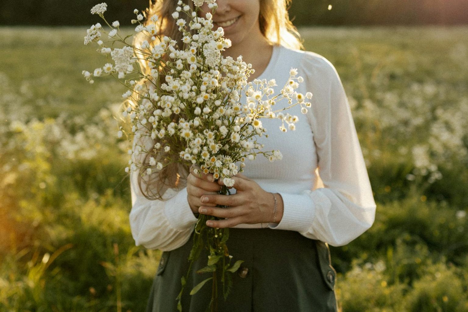 Smiling woman holding a bouquet of wildflowers in a sunlit meadow.