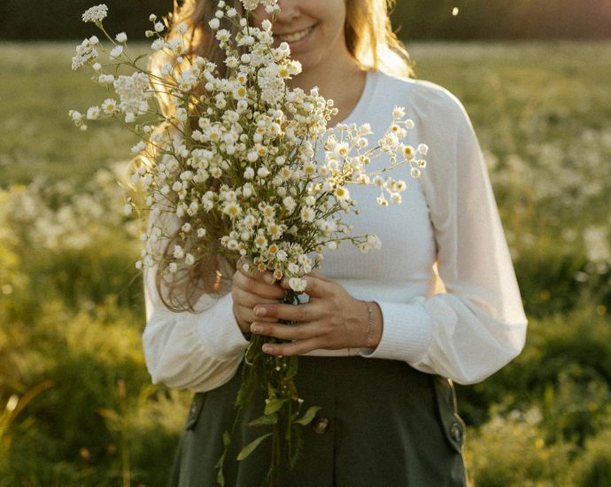 Smiling woman holding a bouquet of wildflowers in a sunlit meadow.