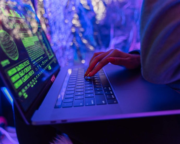 Close-up of hands typing on a laptop displaying cybersecurity graphics, illuminated by purple light.