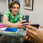 A student sharing his phone screen with another in a classroom setting.
