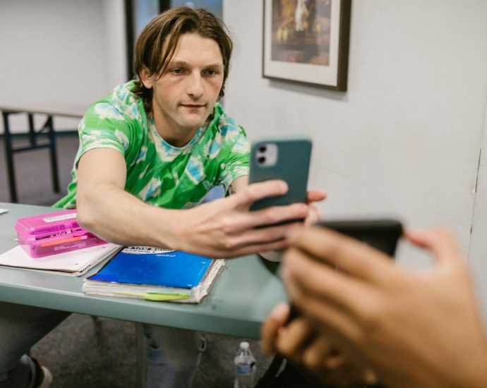 A student sharing his phone screen with another in a classroom setting.