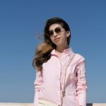 Woman smiles in sunglasses, against a bright blue sky.