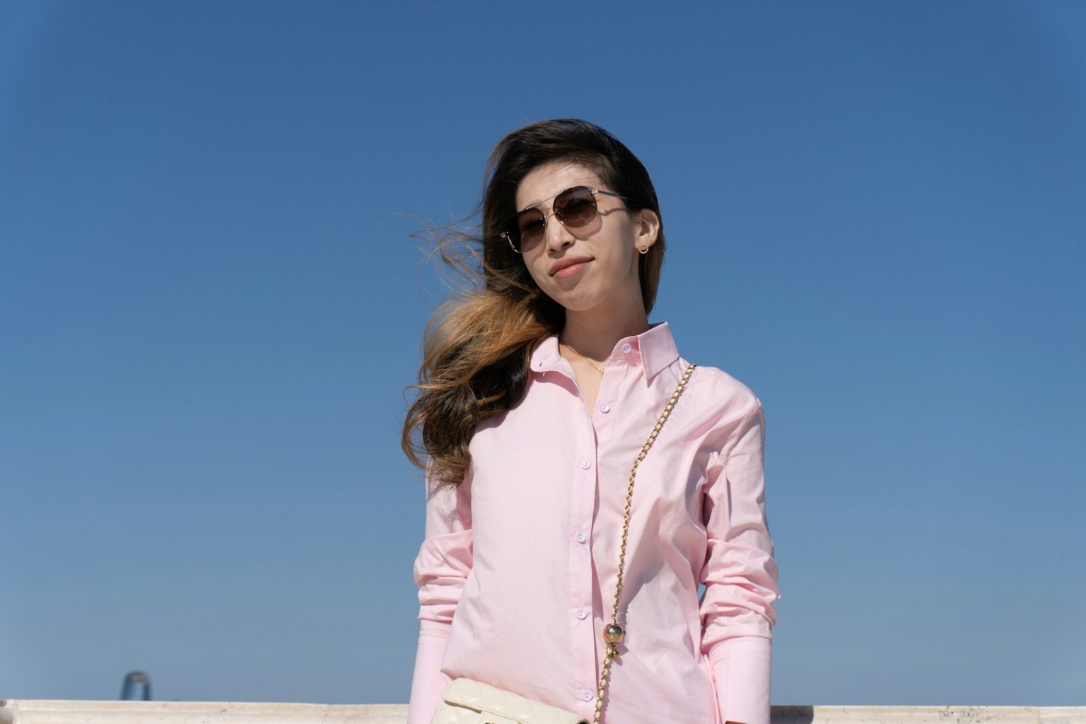 Woman smiles in sunglasses, against a bright blue sky.