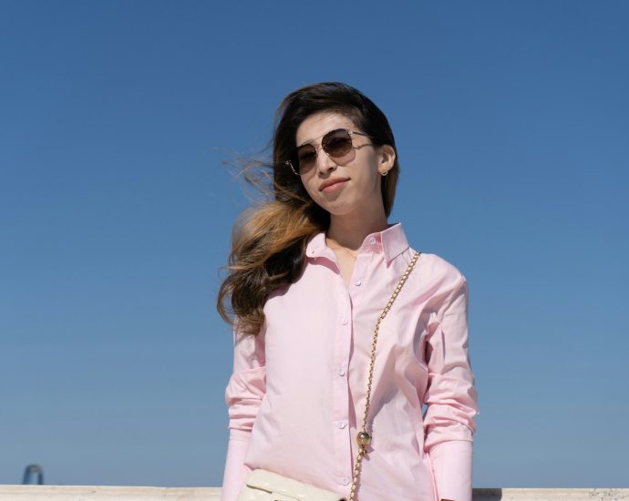Woman smiles in sunglasses, against a bright blue sky.