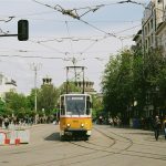 a yellow and white train traveling down a street next to tall buildings