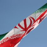 two flags flying in the wind with a blue sky in the background