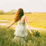 A woman walks away through a grassy field.