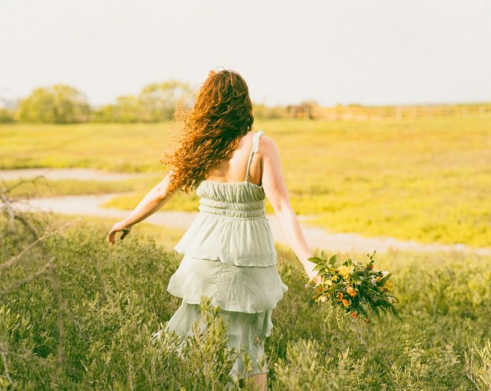 A woman walks away through a grassy field.
